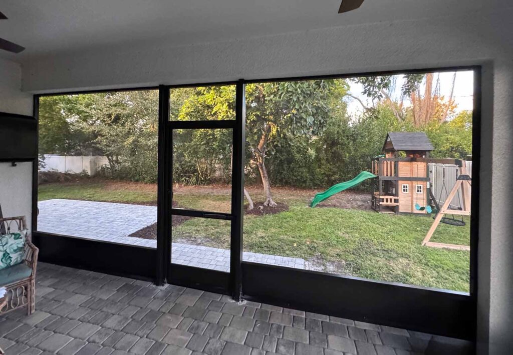 view looking through a screened back porch with a paver floor and kids playset in the background